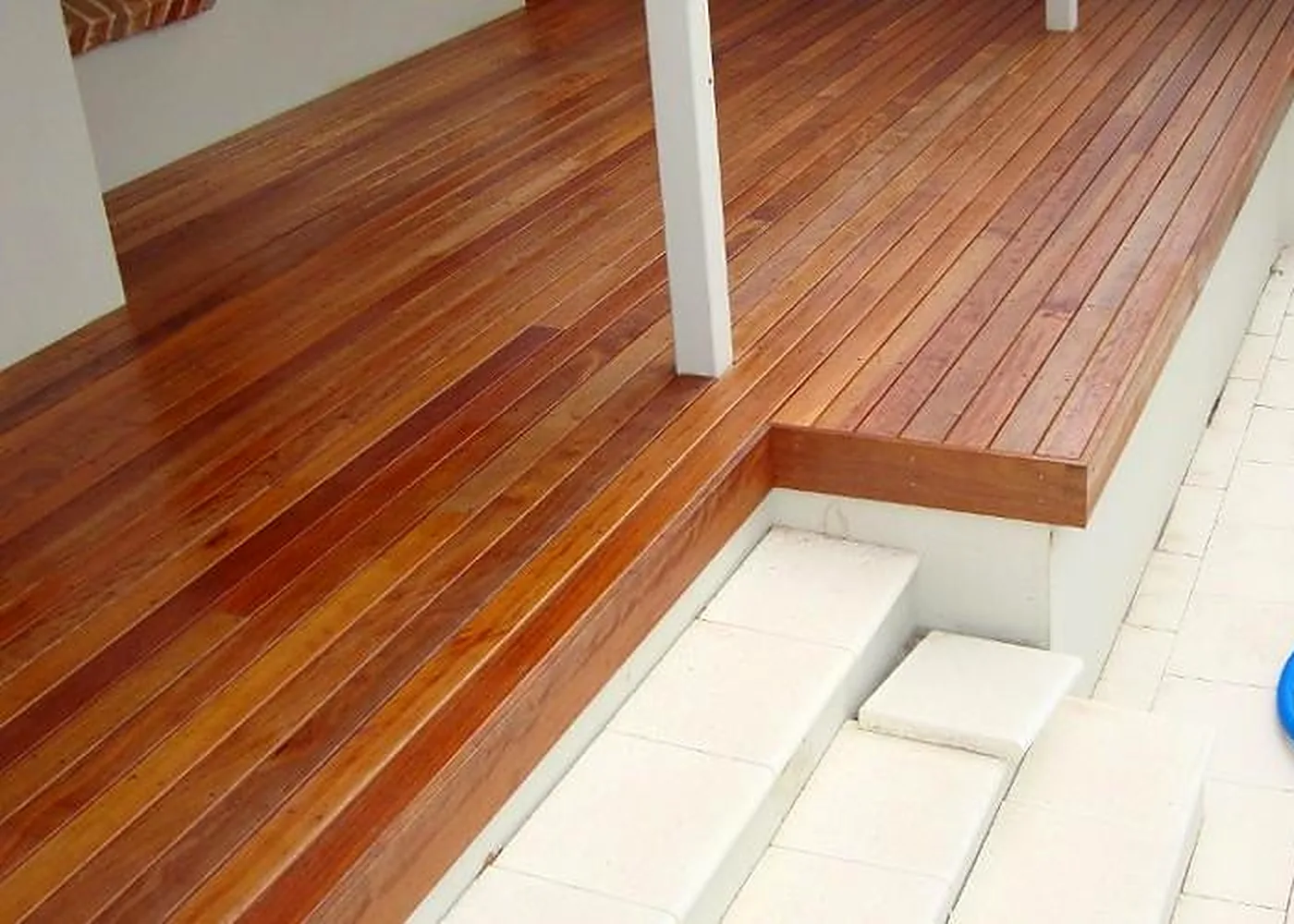 Freshly oiled hardwood deck wrapping a corner with a raised edge over pale paving and steps