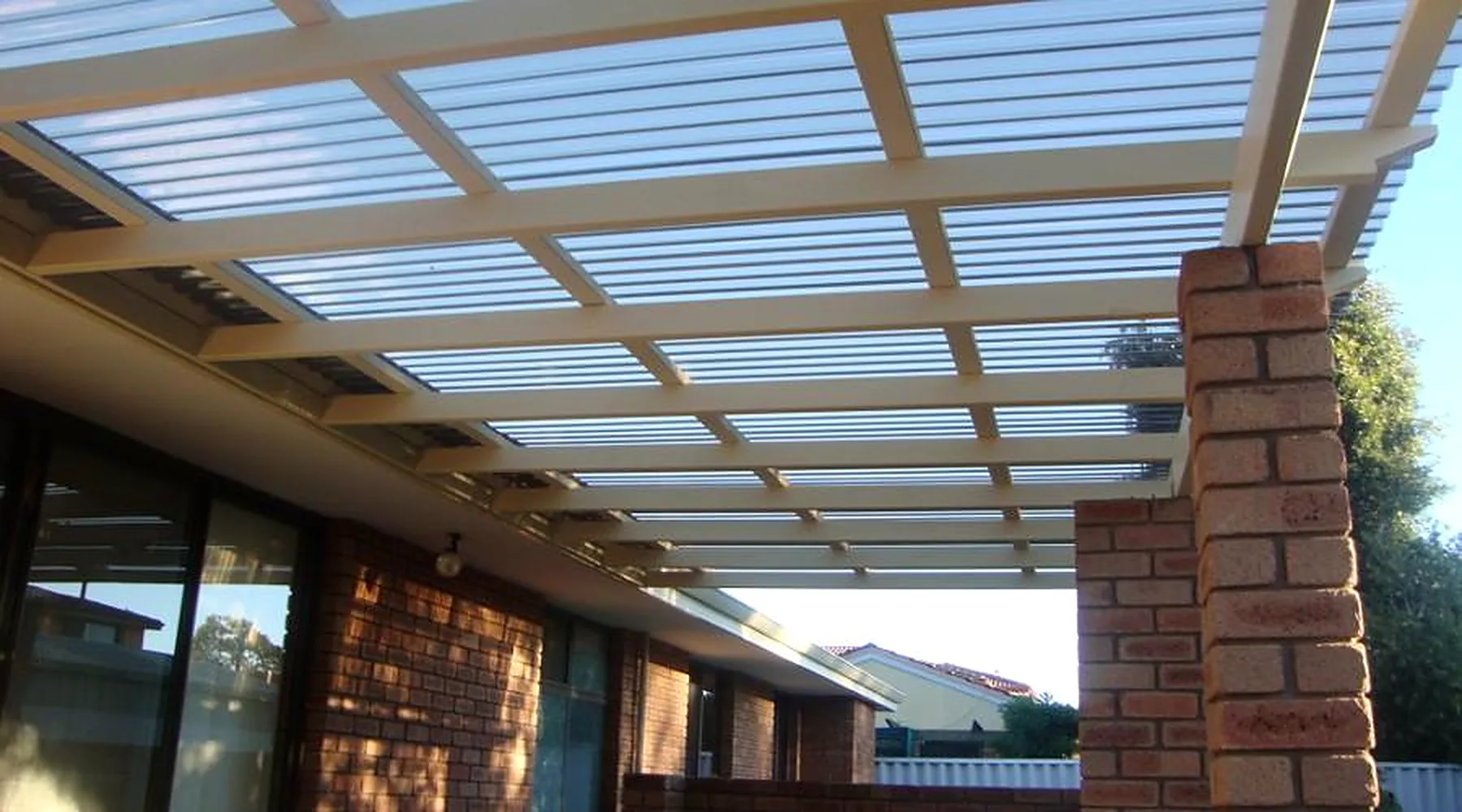 Painted pergola with clear corrugated roofing fixed to a red brick pier